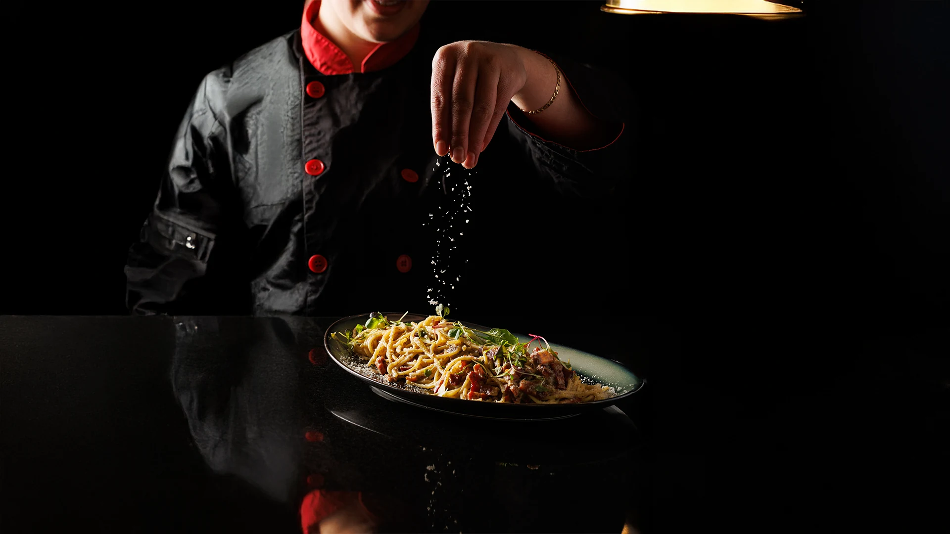 Chef finishing pasta in a dark kitchen scene